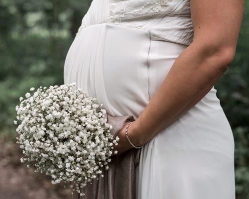 A closeup shot of a pregnant bride holding a white bouquet on her wedding day