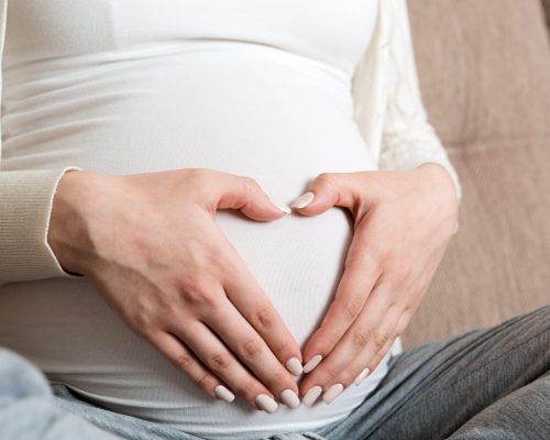 Young pregnant woman holds wooden heart. Love concept.